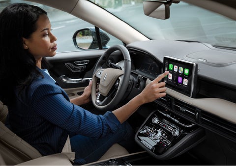 A woman in the driver's seat of a 2022 Lincoln Corsair is touching the center digital screen to connect to Apple CarPlay® | Maguire's Lincoln in Palmyra PA