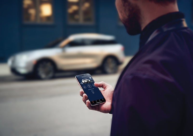 A person is shown interacting with a smartphone to connect to a Lincoln vehicle across the street. | Maguire's Lincoln in Palmyra PA